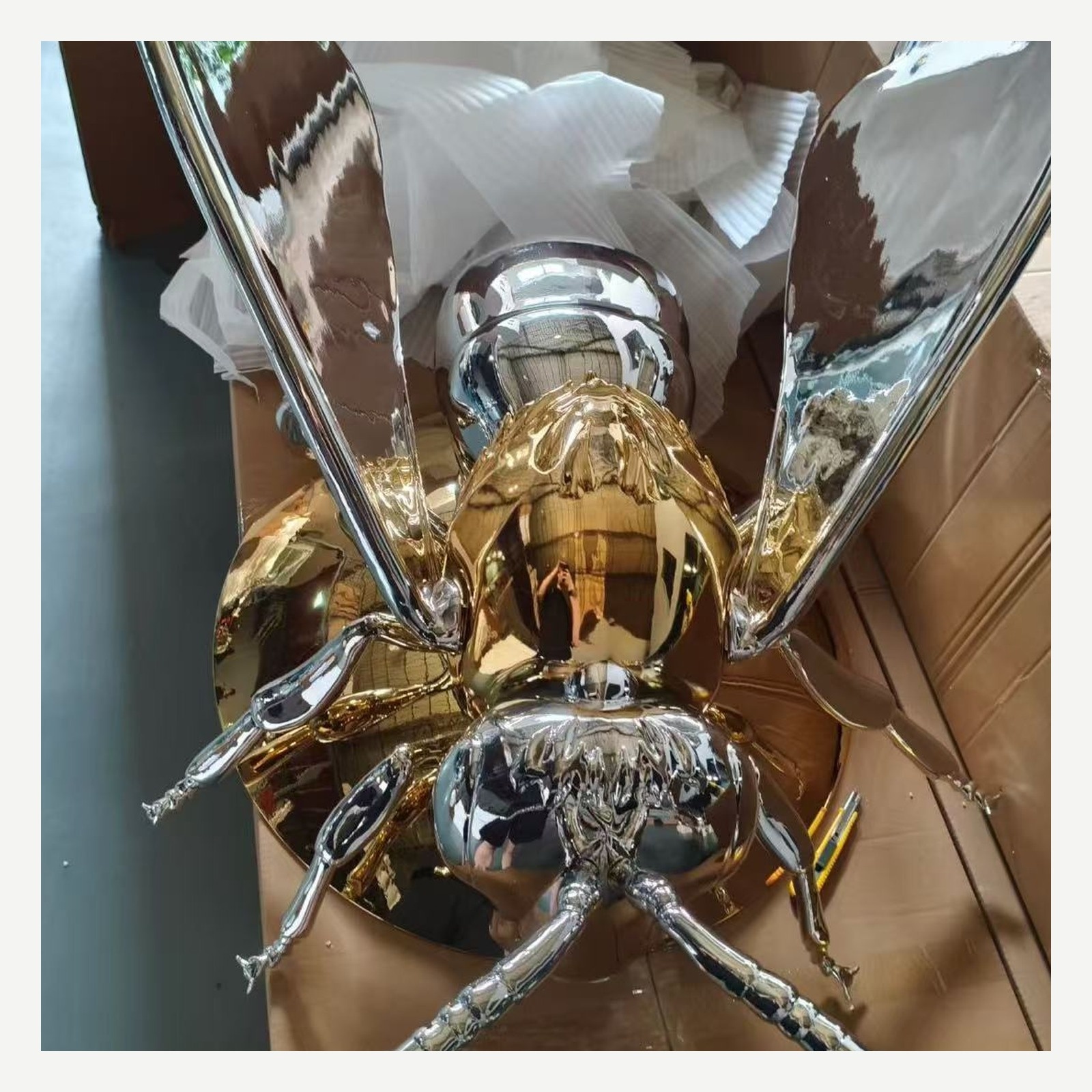 Chrome and gold winged insect sculpture viewed from the side