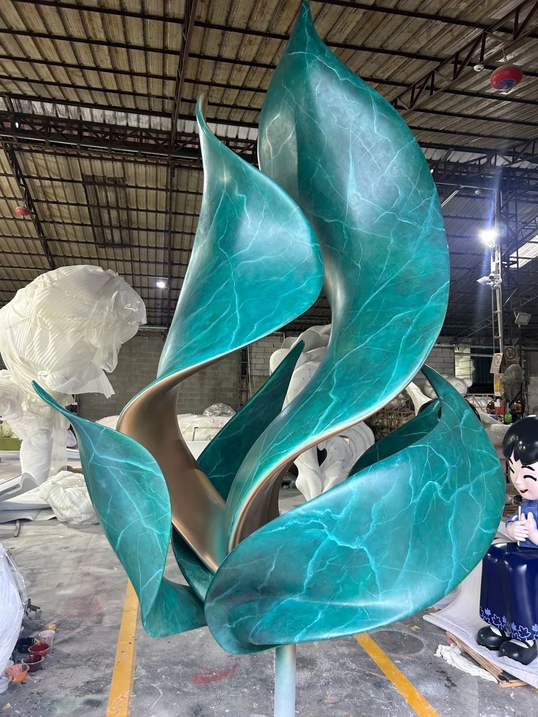 Three-quarter workshop view of the same stainless steel leaf sculpture