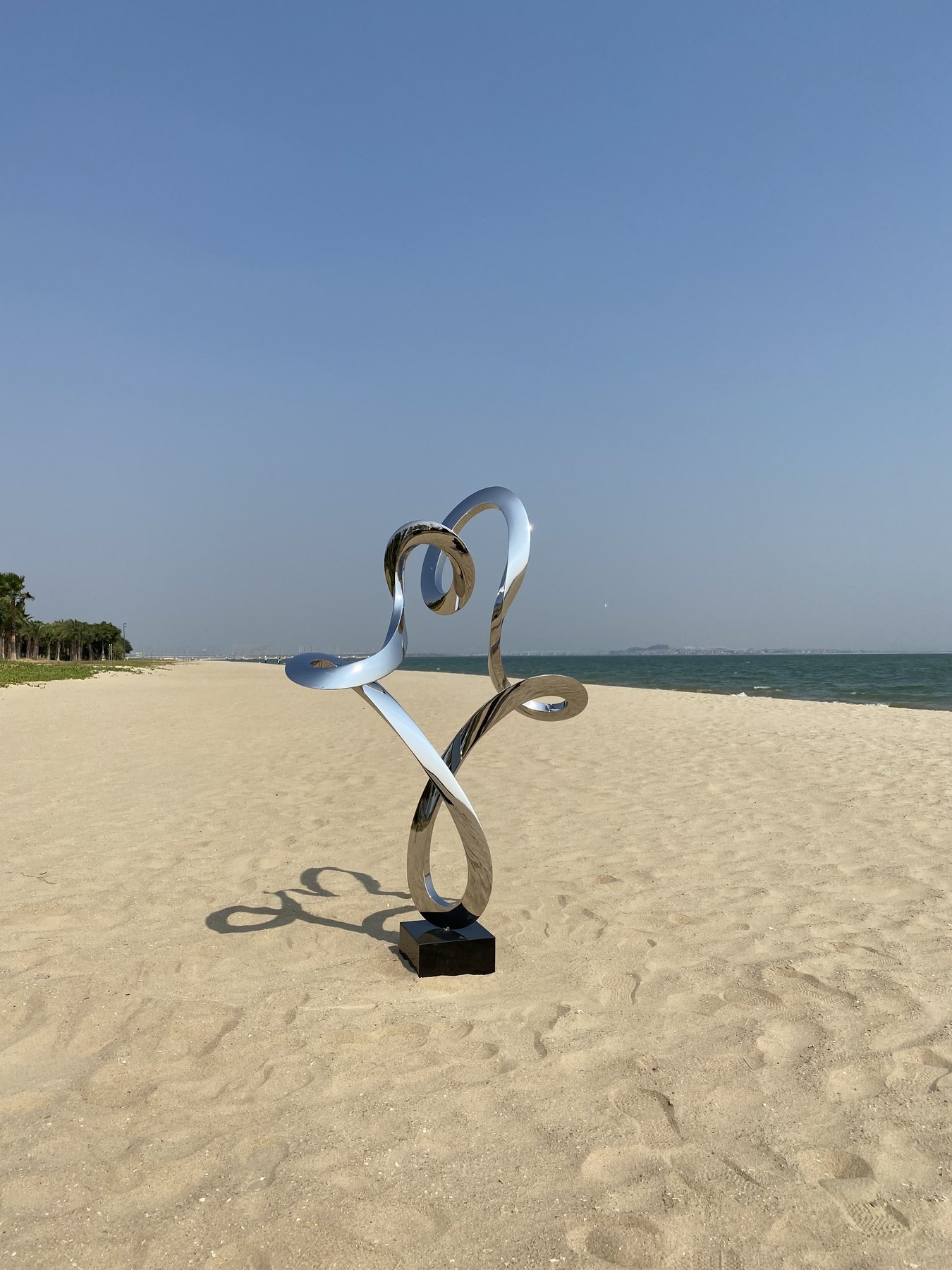 Full coastal view of the same mirror stainless steel abstract figure sculpture