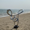 Mirror stainless steel flowing loop sculpture in a coastal landscape