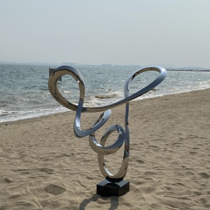 Mirror stainless steel flowing loop sculpture in a coastal landscape